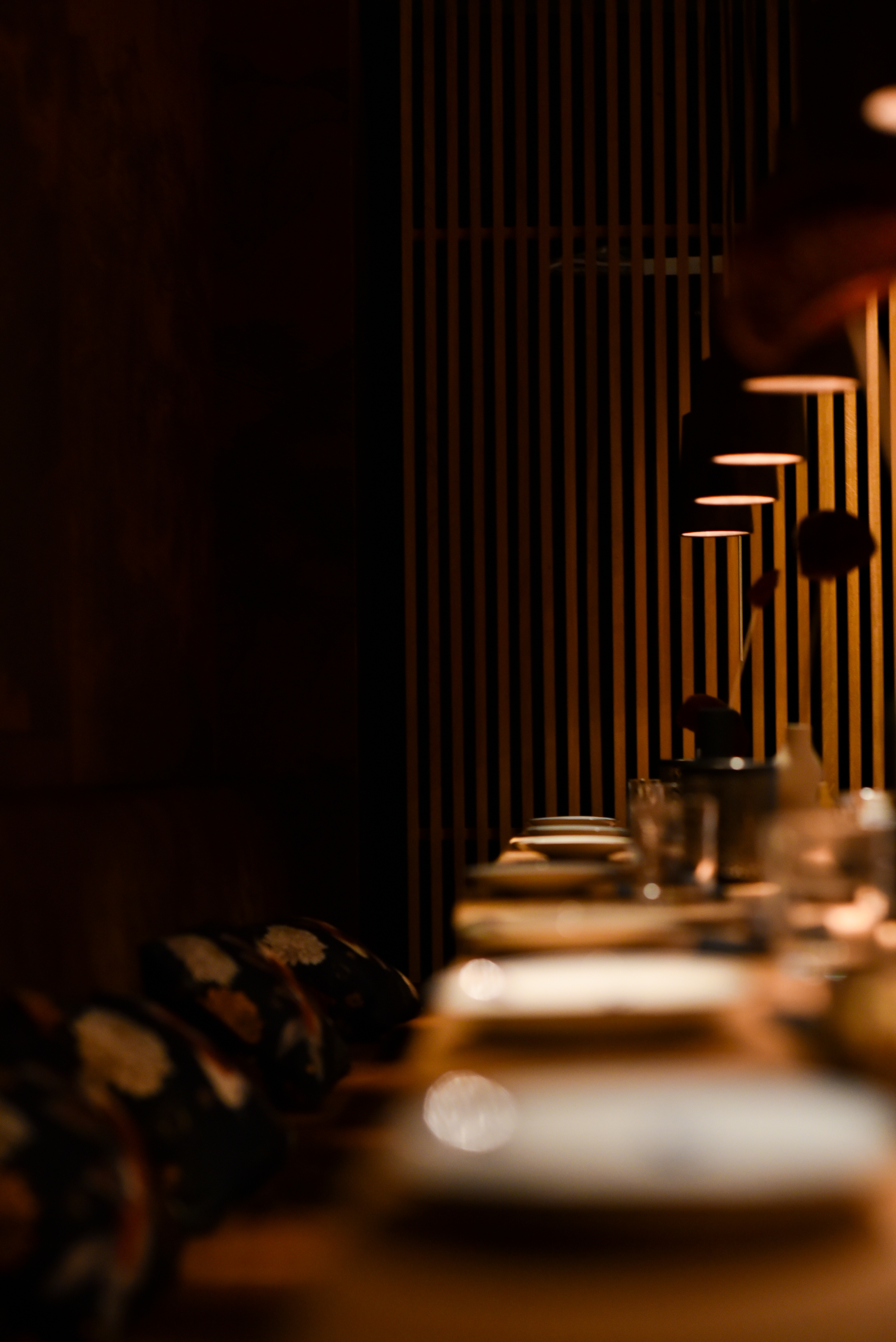 Bar de restaurant en pierre sur mesure, au fond étagères murales rétroéclairées, structure métal et verres, assises tapissées en velours