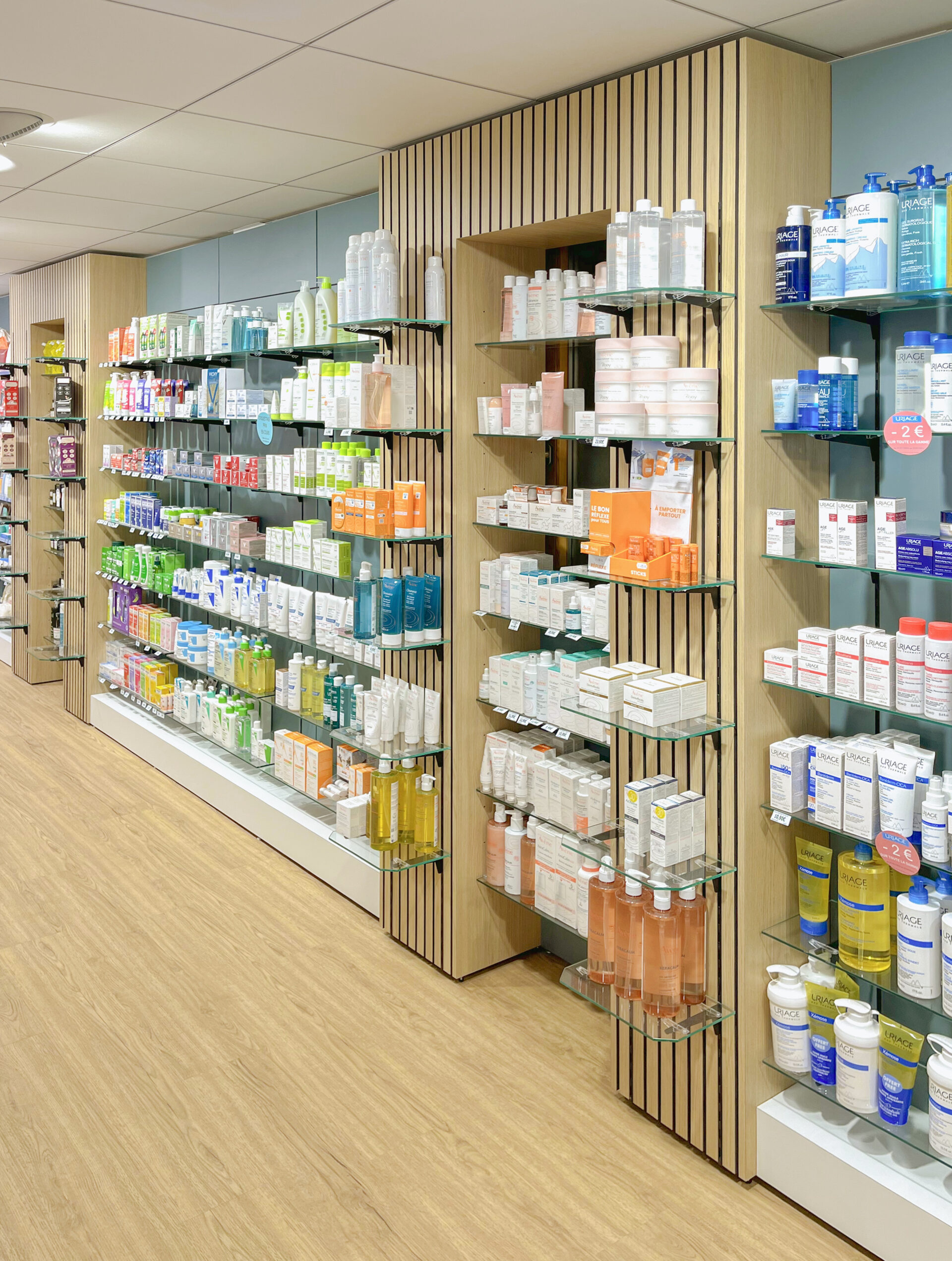 Linéaire de pharmacie avec étagères murales en verre et habillage bois à lames verticales sur mesure